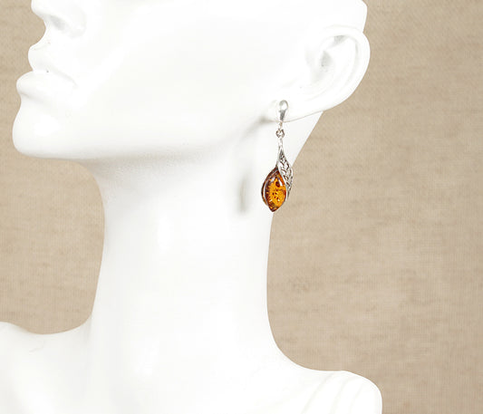 Teardrop-shaped amber earrings on a white mannequin head against a beige background