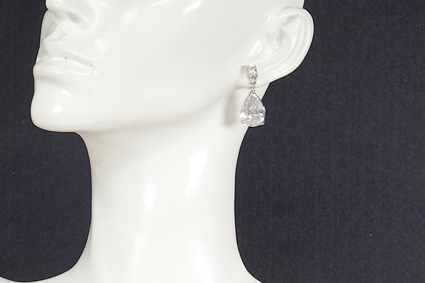 Silver teardrop earrings on a white mannequin ear against a black background
