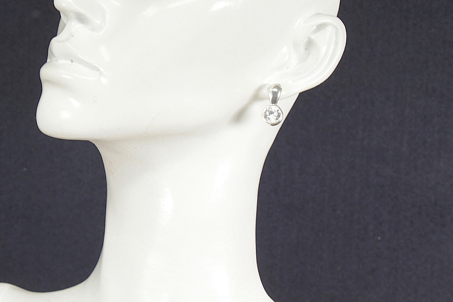 Silver earring with a clear gemstone on a mannequin head against a black background