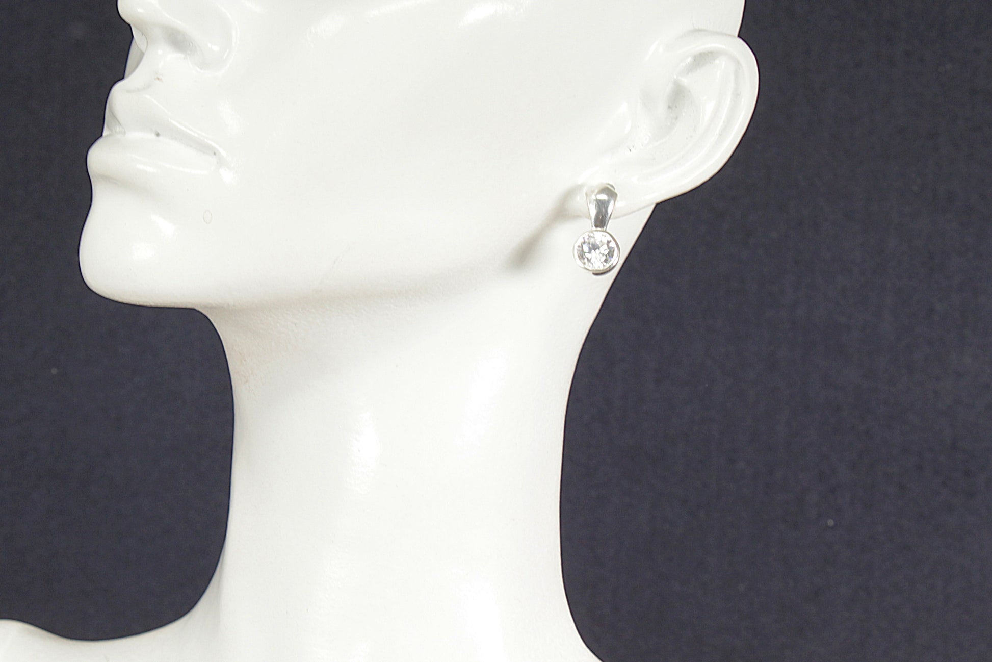 Silver earring with a clear gemstone on a mannequin head against a black background