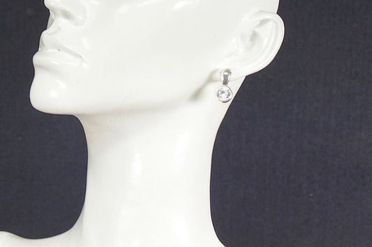 Silver earring with a clear gemstone on a mannequin head against a black background