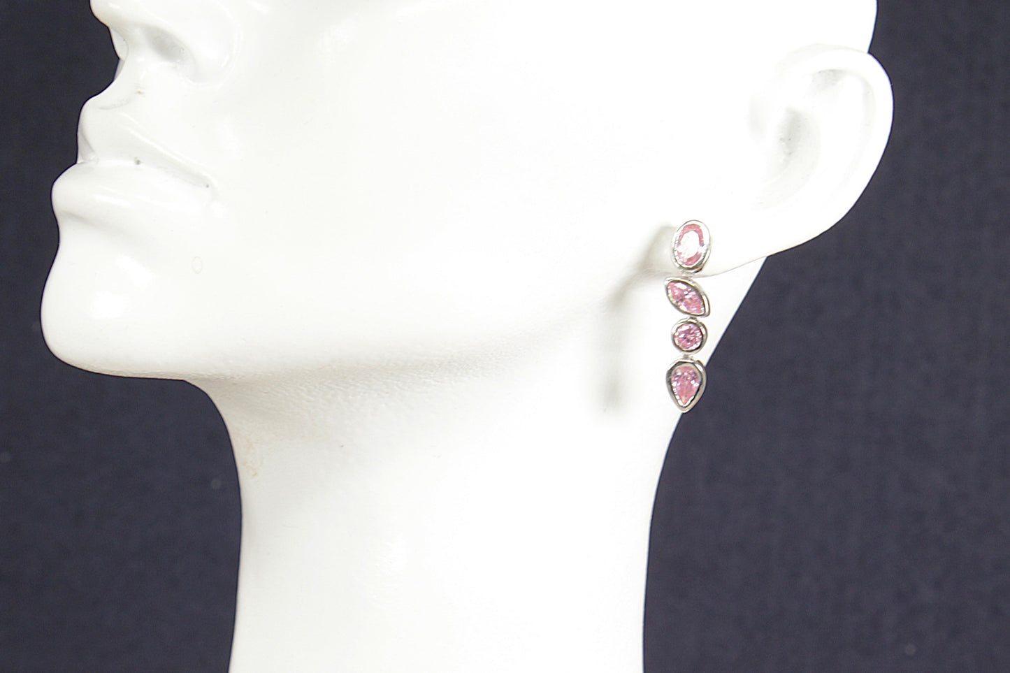 Pink earrings on a white mannequin ear against a dark background