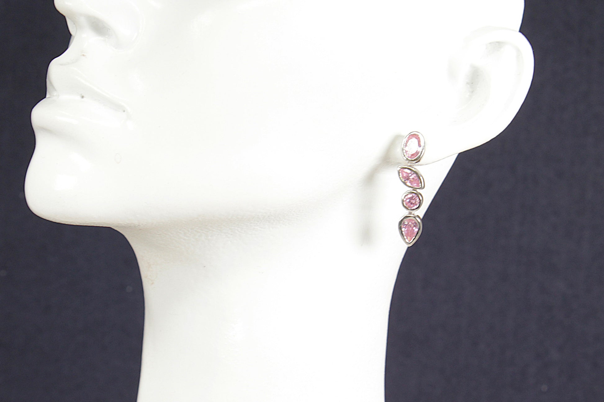 Pink earrings on a white mannequin ear against a dark background