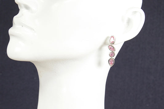 Pink earrings on a white mannequin ear against a dark background