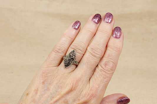 Hand wearing a decorative art deco marcasite ring with pink glittery nails on a beige background