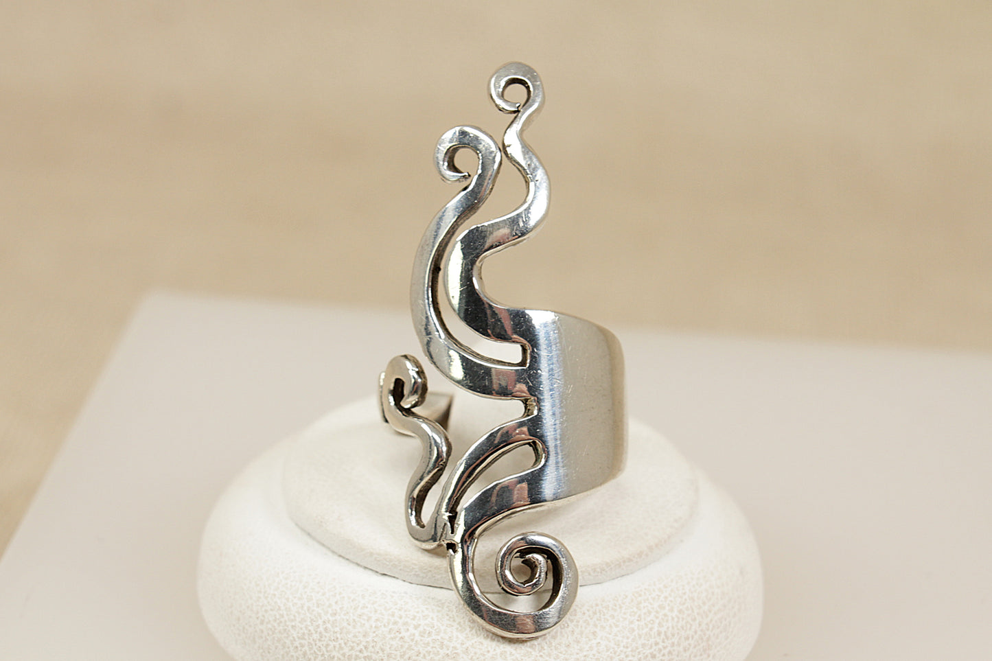 Silver ring with intricate design on a white stand against a beige background