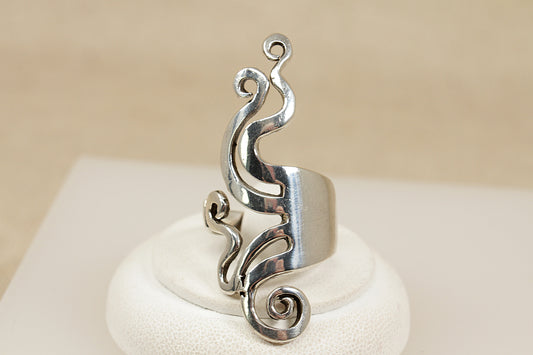 Silver ring with intricate design on a white stand against a beige background