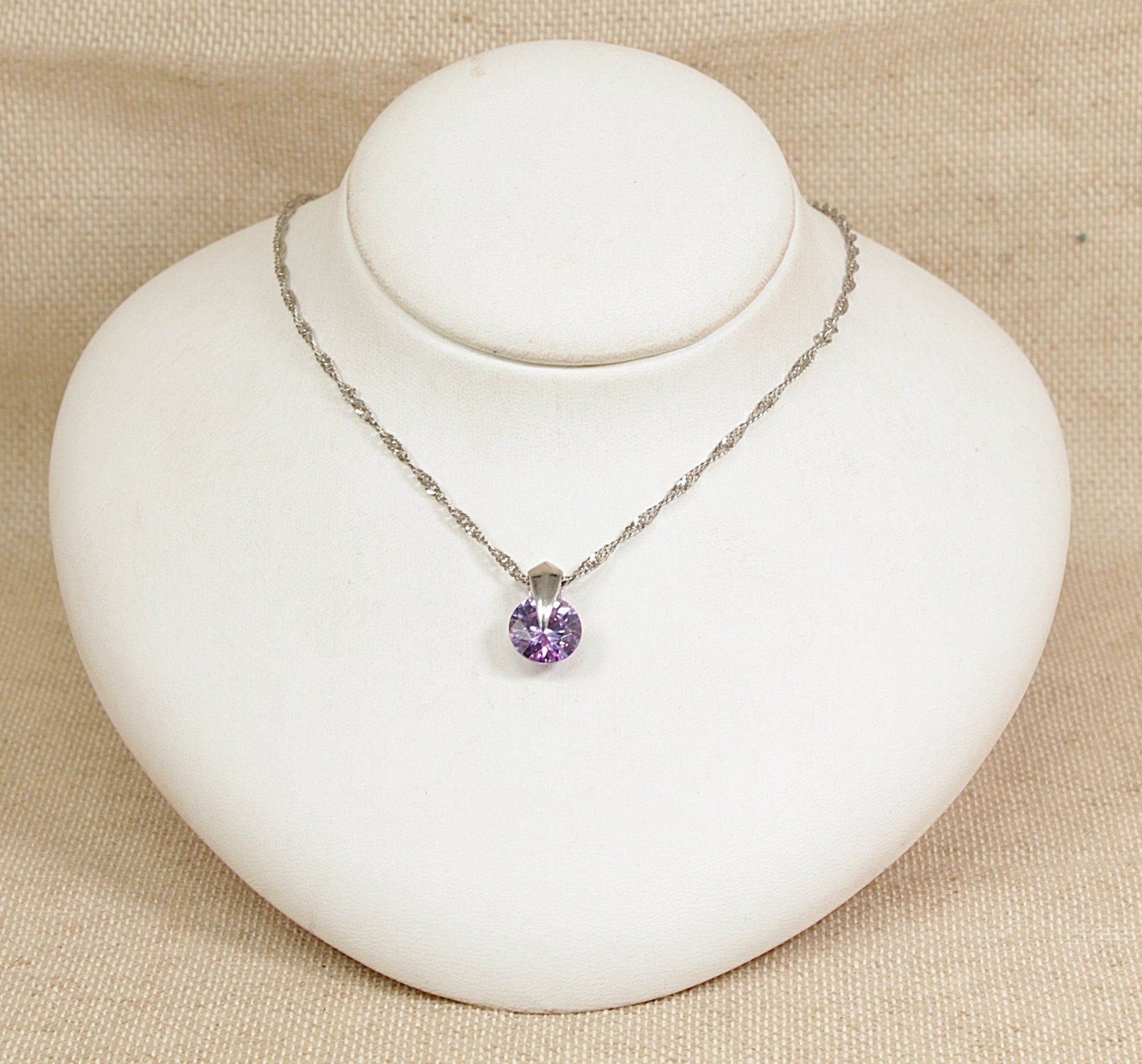 Necklace with a purple round-shaped pendant on a white bust against a beige background