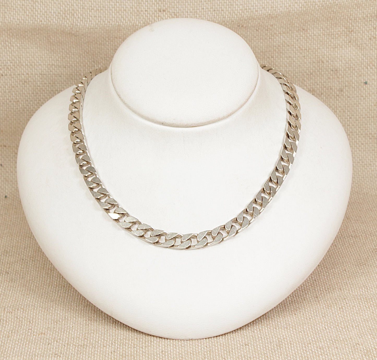 Silver chain necklace on a white bust against a beige background