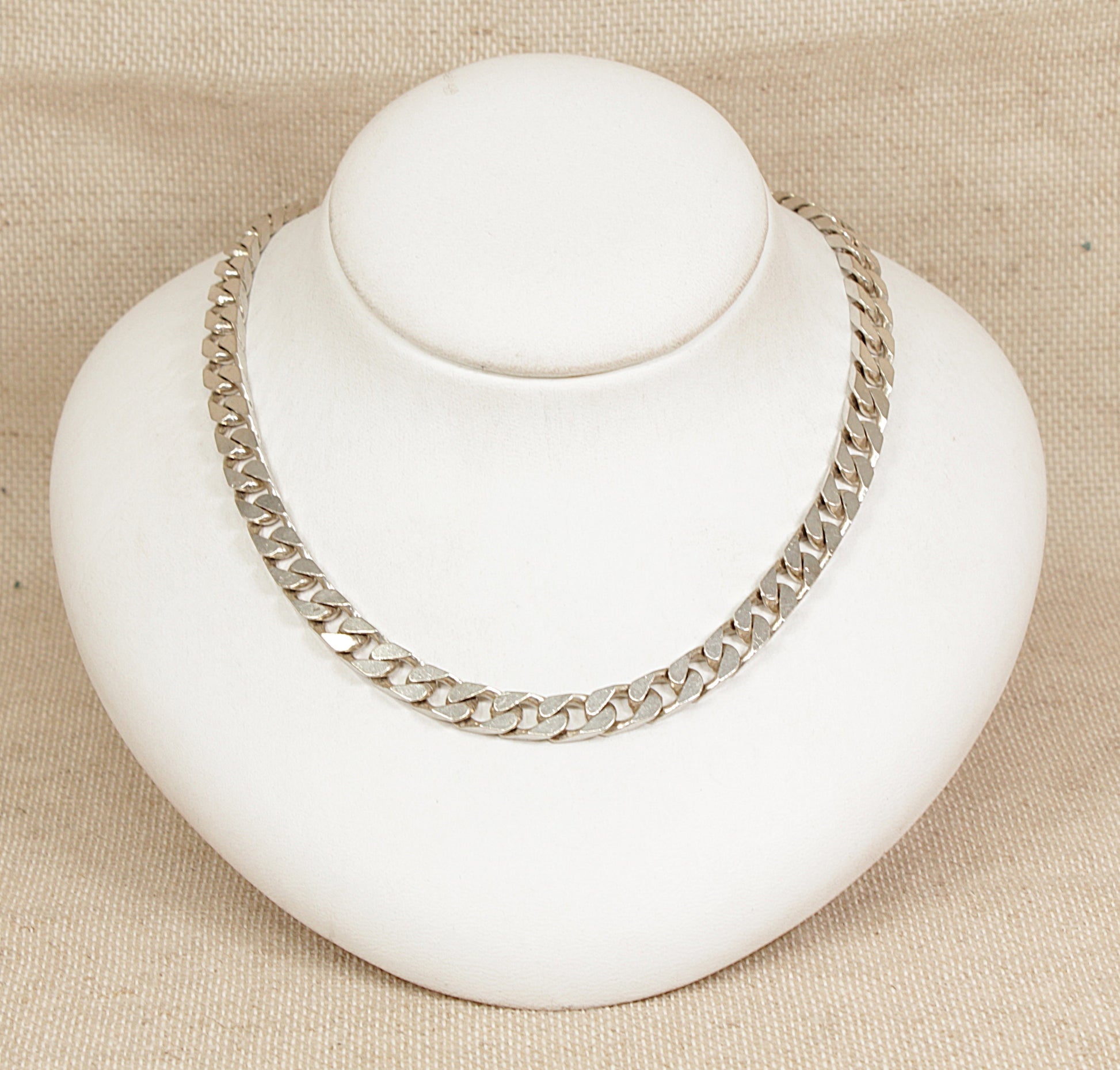 Silver chain necklace on a white bust against a beige background