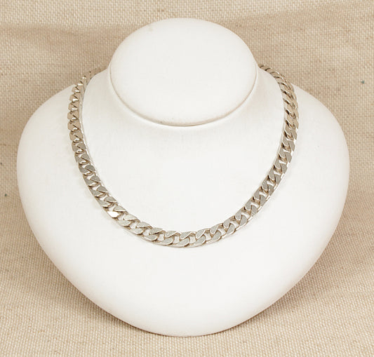 Silver chain necklace on a white bust against a beige background