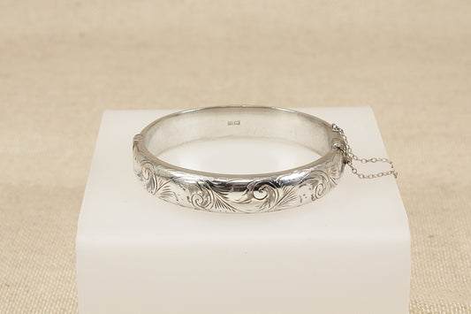 Vintage Antique Silver bracelet bangle with intricate design on a white cube against a beige background