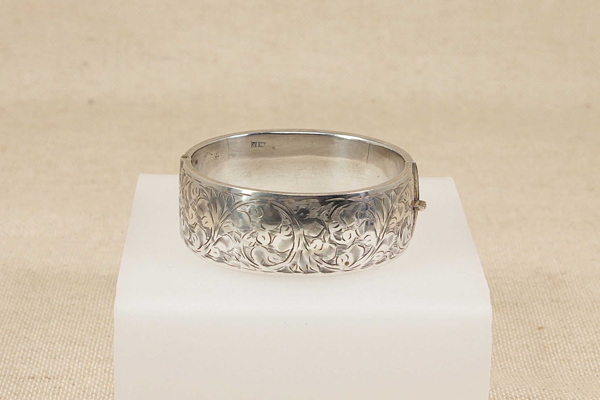 Vintage antique Silver bracelet bangle  with intricate design on a white pedestal against a beige background