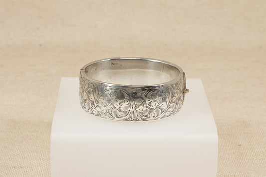 Vintage antique Silver bracelet bangle  with intricate design on a white pedestal against a beige background