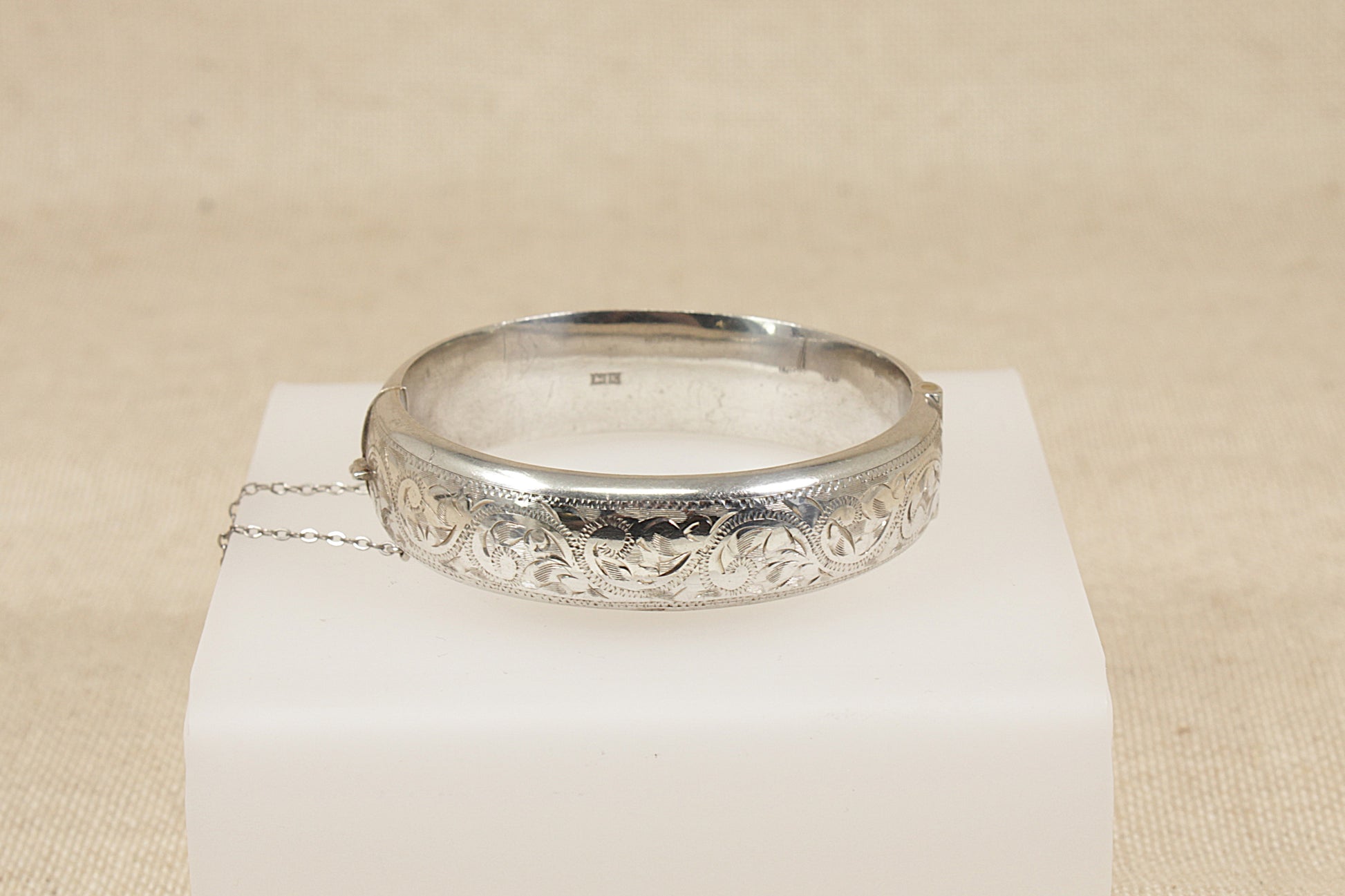 Vintage antique Silver bracelet bangle  with intricate design on a white stand against a beige background