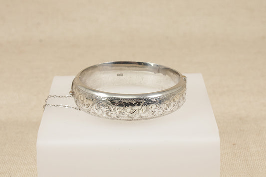 Vintage antique Silver bracelet bangle  with intricate design on a white stand against a beige background