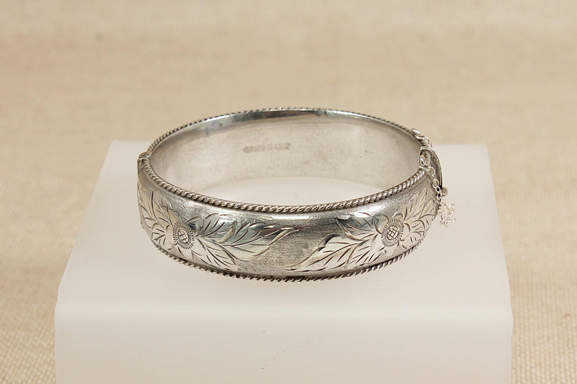 Silver bracelet with engraved design on a beige background