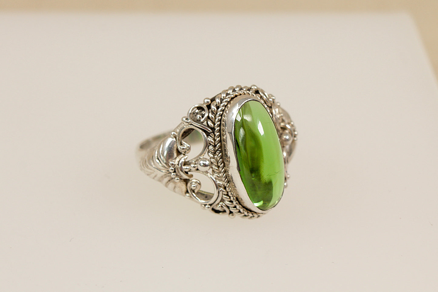 Silver statement ring with a green gemstone on a beige background