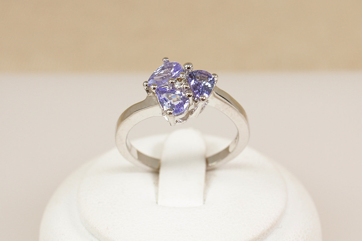 Silver ring with heart-shaped gemstones on a white stand against a beige background