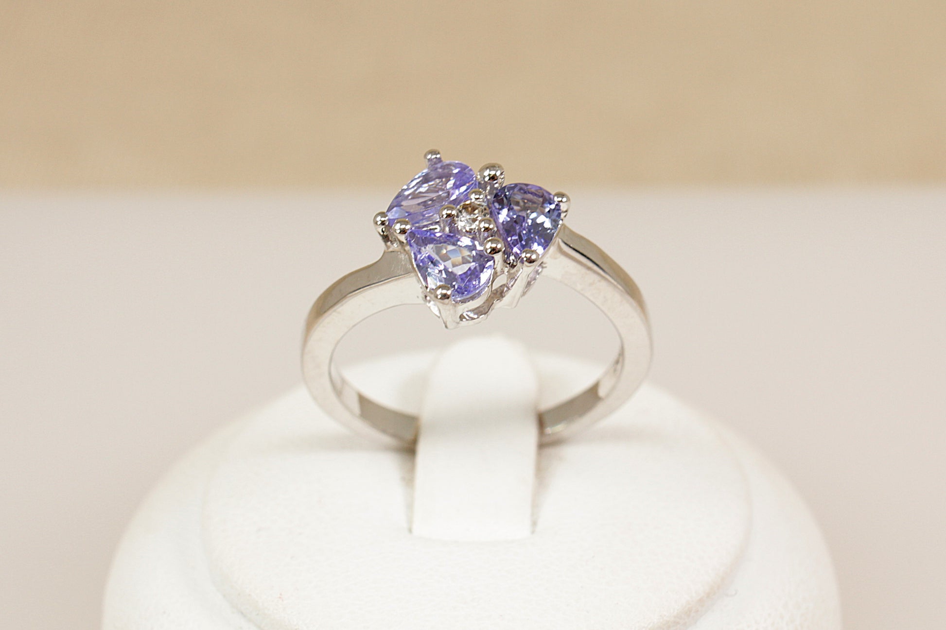 Silver ring with heart-shaped gemstones on a white stand against a beige background