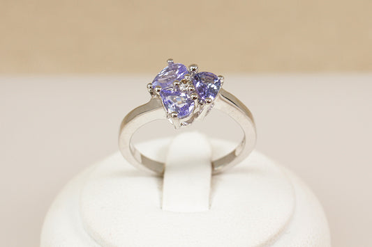 Silver ring with heart-shaped gemstones on a white stand against a beige background