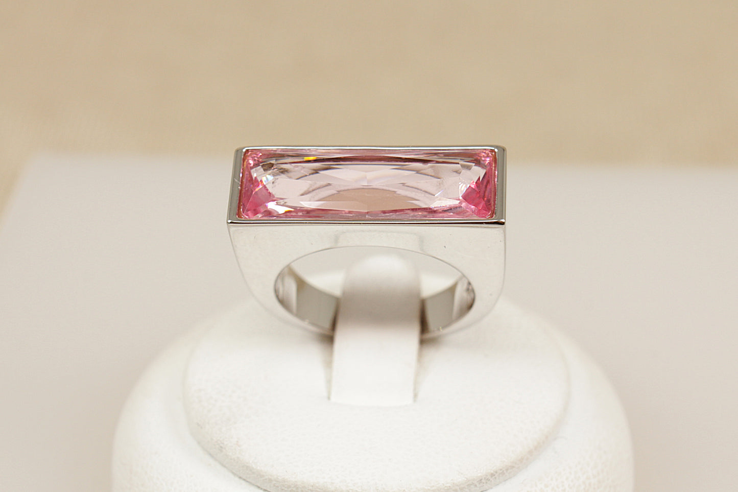Swarovski ring with a pink gemstone on a white stand against a beige background