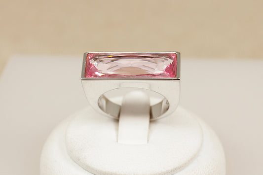 Swarovski ring with a pink gemstone on a white stand against a beige background
