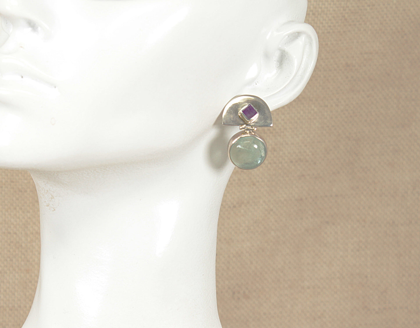 Earring with an aquamarine and amethyst gemstones on a white mannequin ear