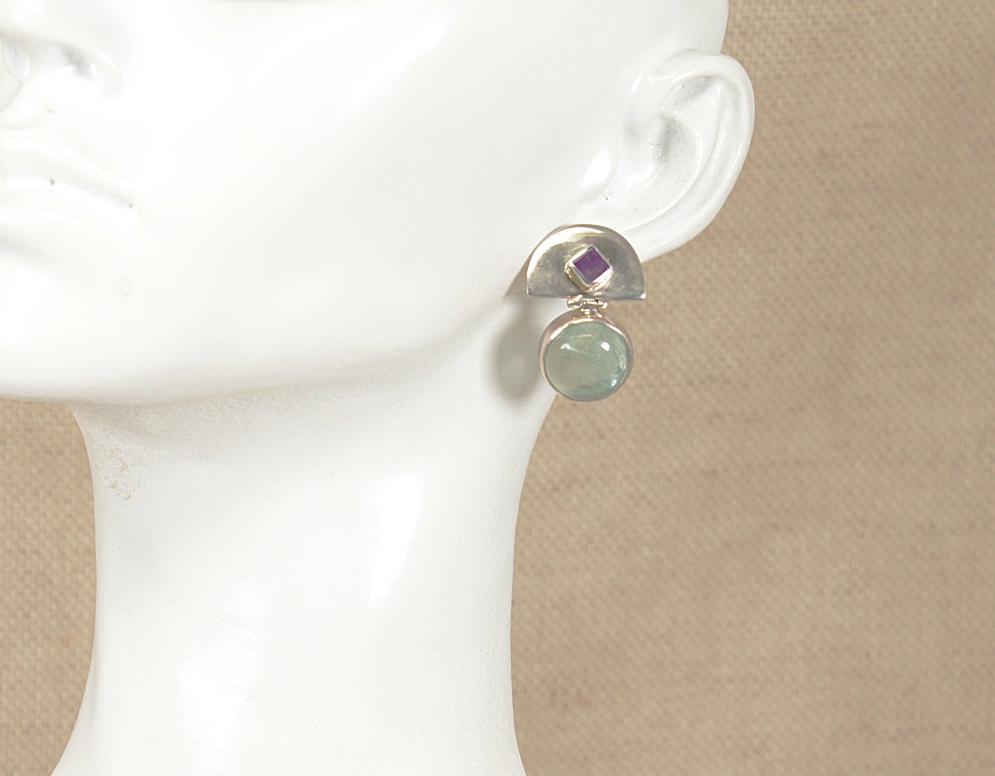 Earring with an aquamarine and amethyst gemstones on a white mannequin ear