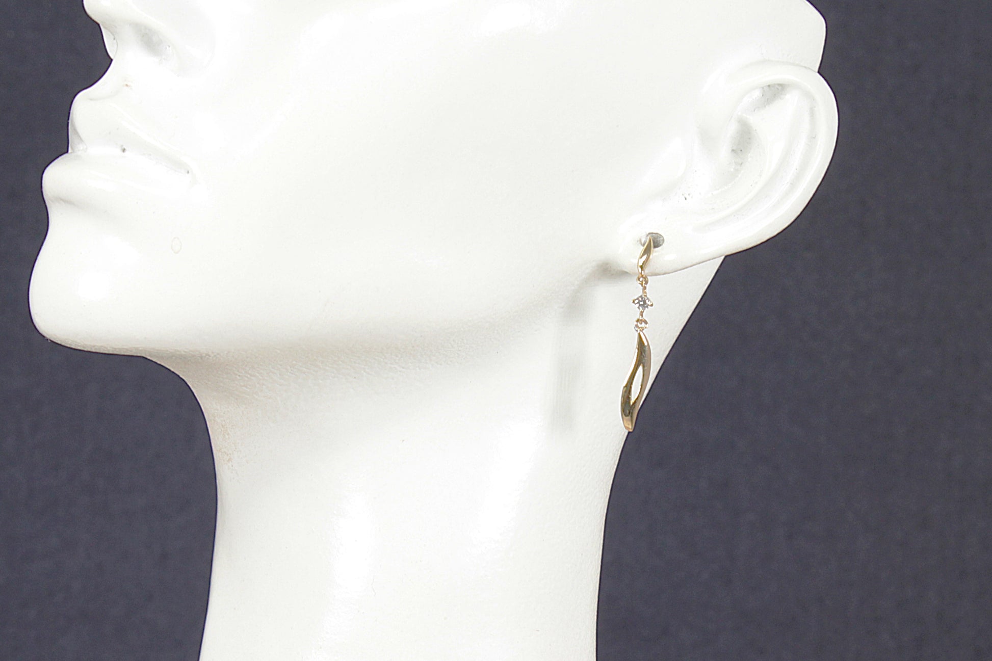 Gold and crystal earrings on a white mannequin head against a dark background