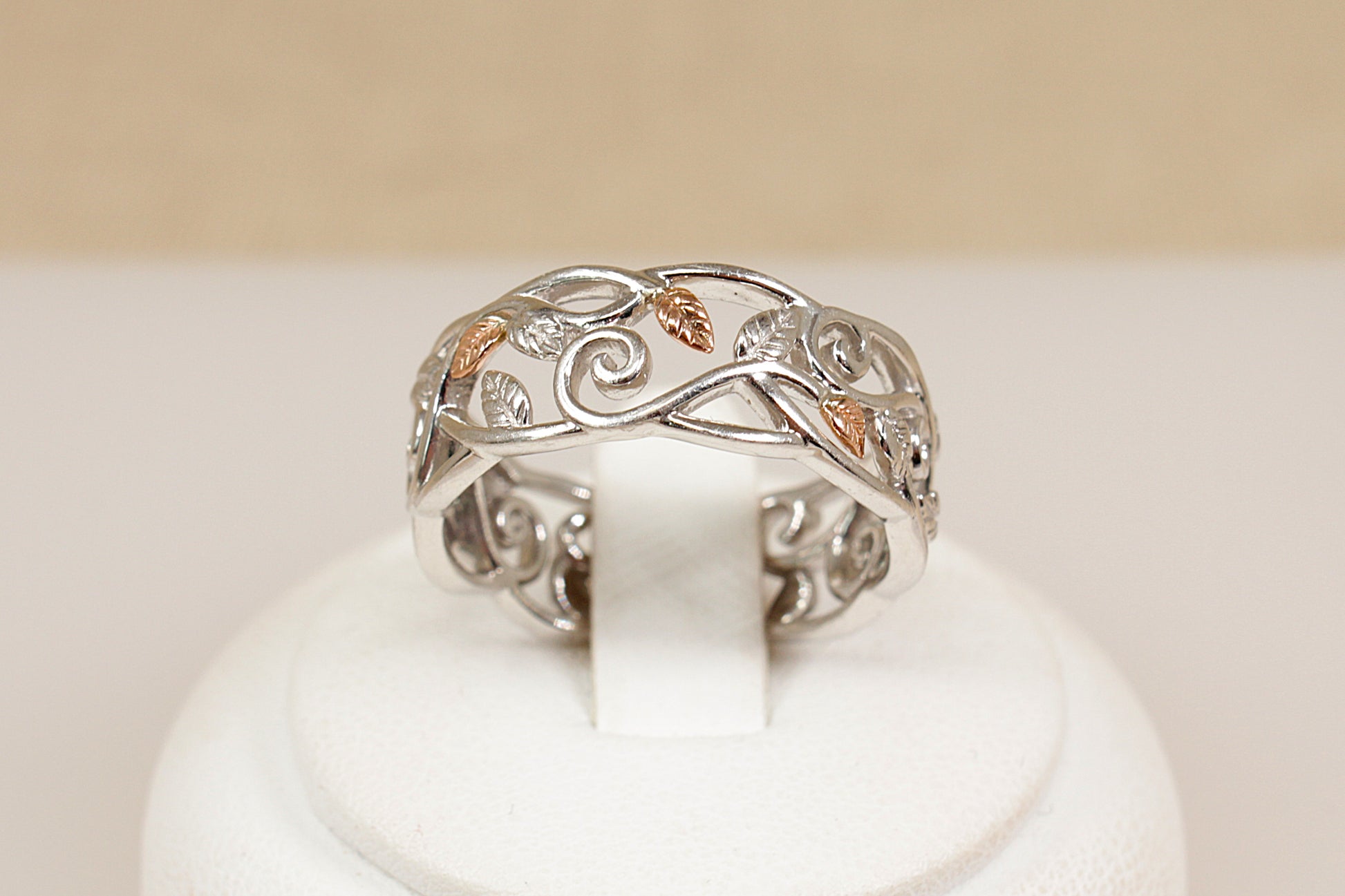Silver ring with intricate designs on a white stand against a beige background