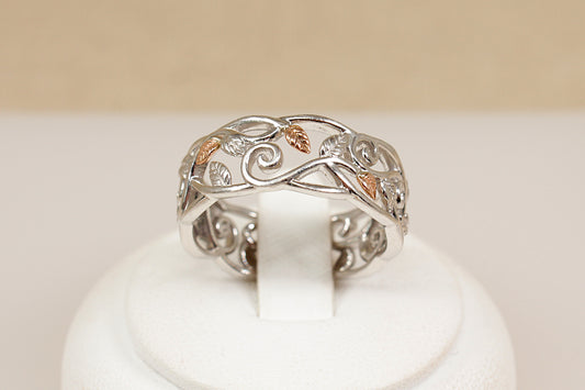 Silver ring with intricate designs on a white stand against a beige background
