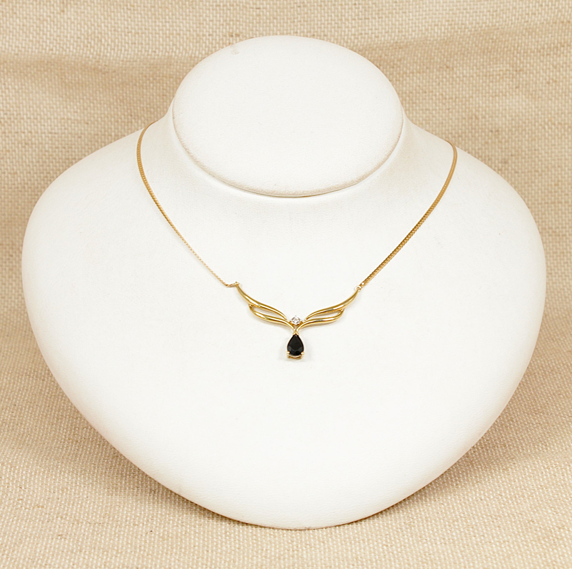 Gold necklace with a blue sapphire  pendant on a white stand against a beige background