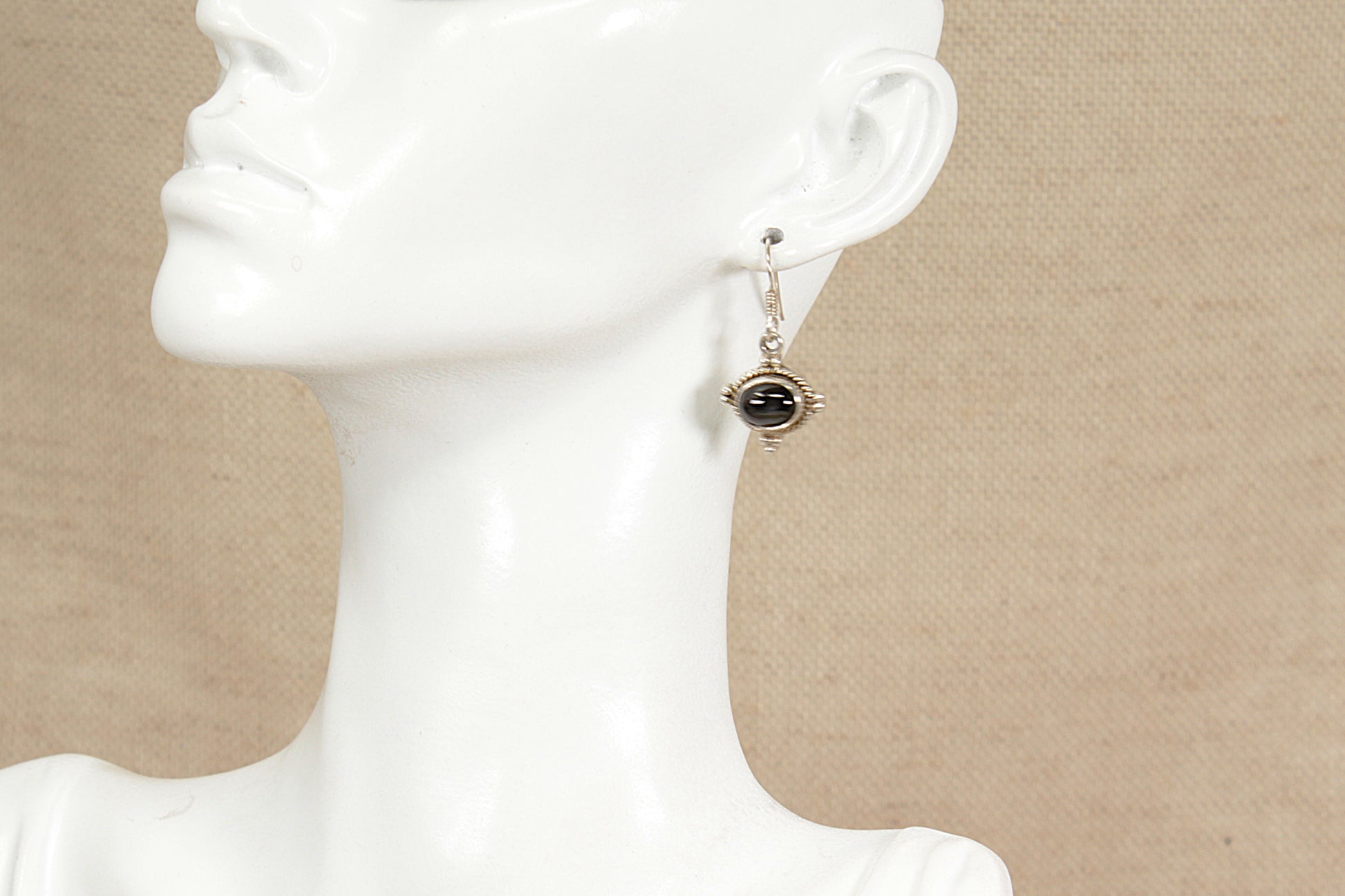 Mannequin wearing a dangling earring with a dark stone on a beige background