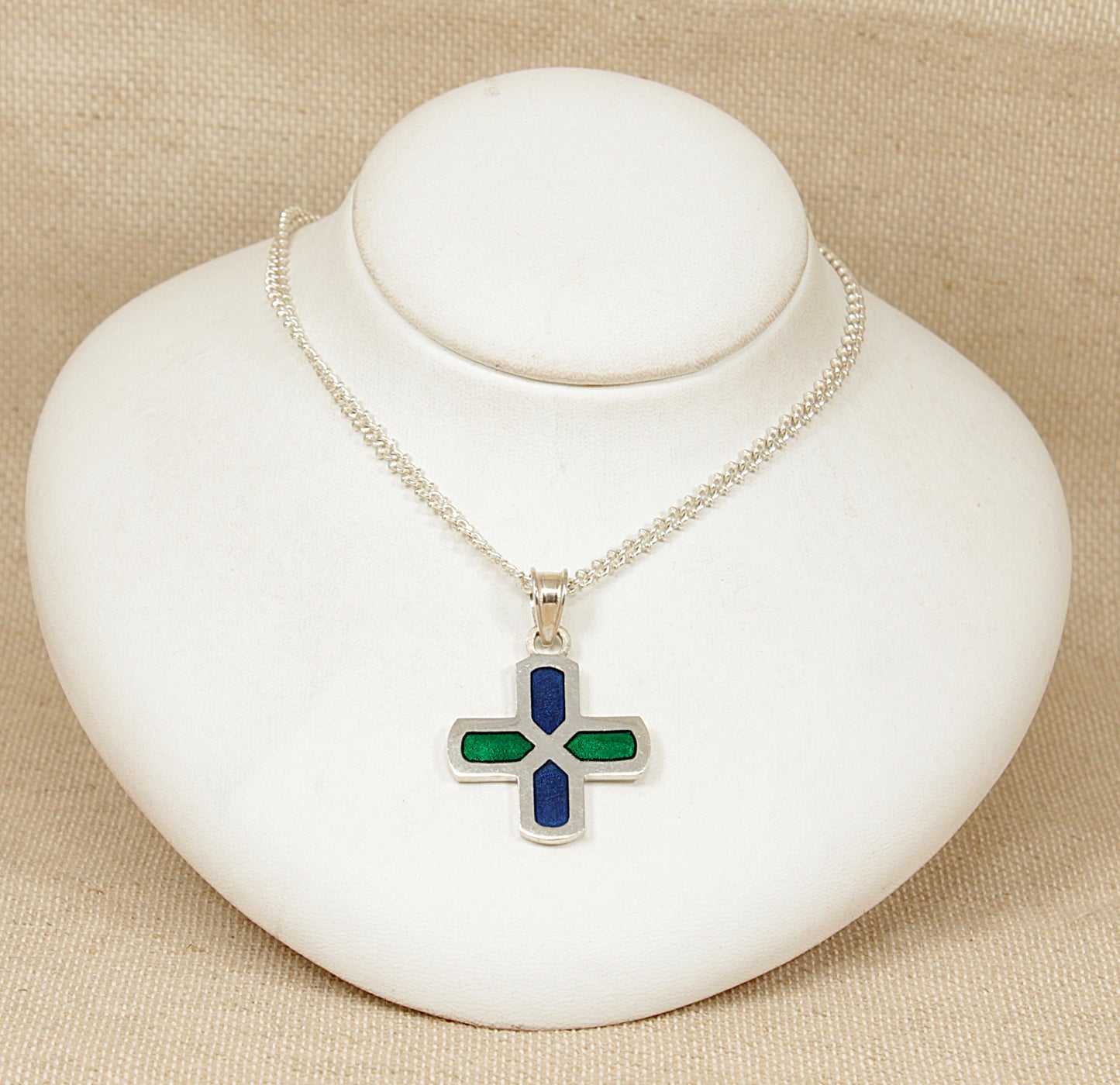 Silver necklace with a cross pendant on a white stand against a beige background