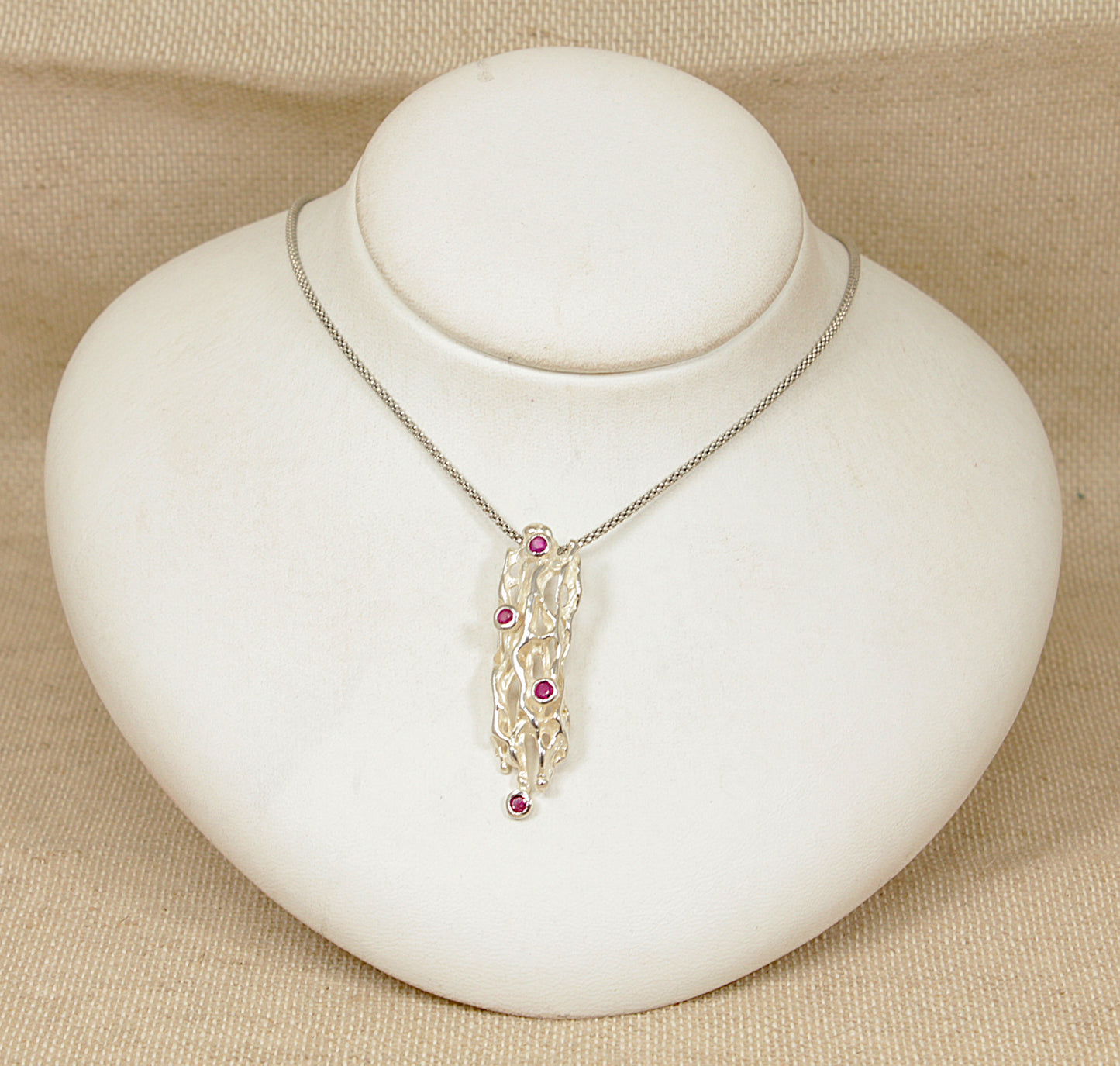 Silver necklace with ruby gemstones on a white jewelry display