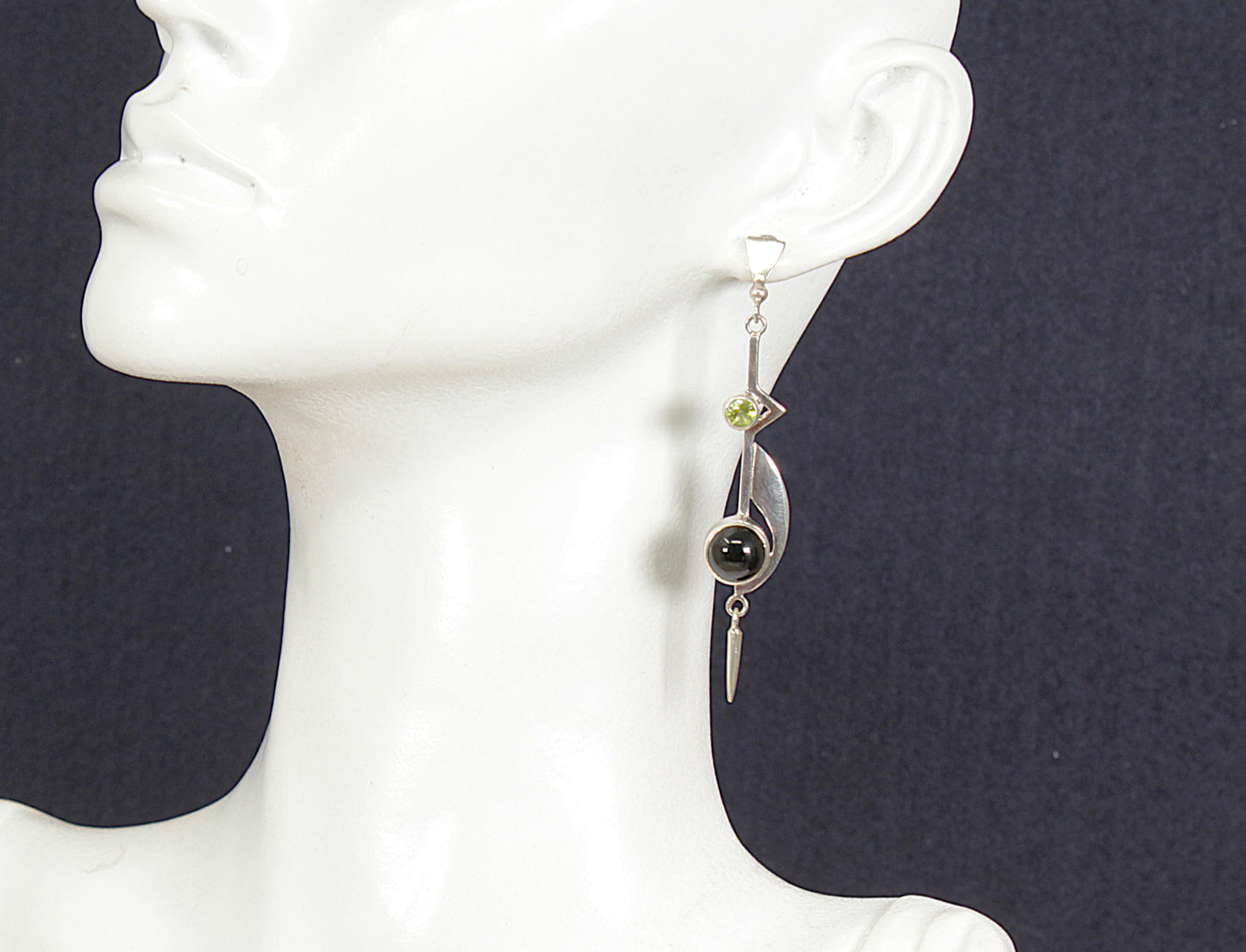 Drop earring with peridot and onyx gemstones on a mannequin ear with a dark background