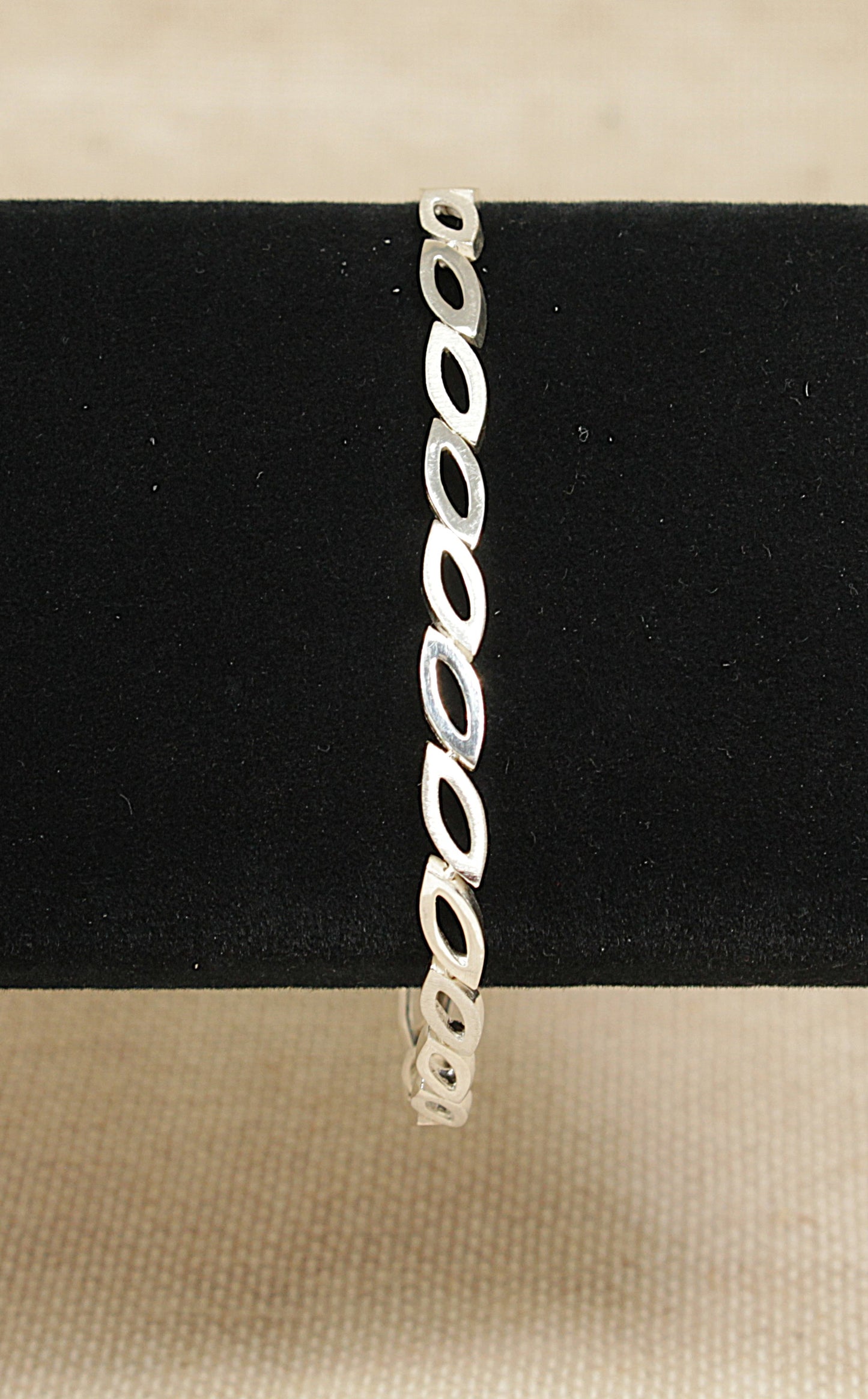 Silver bracelet on a black stand with a beige background