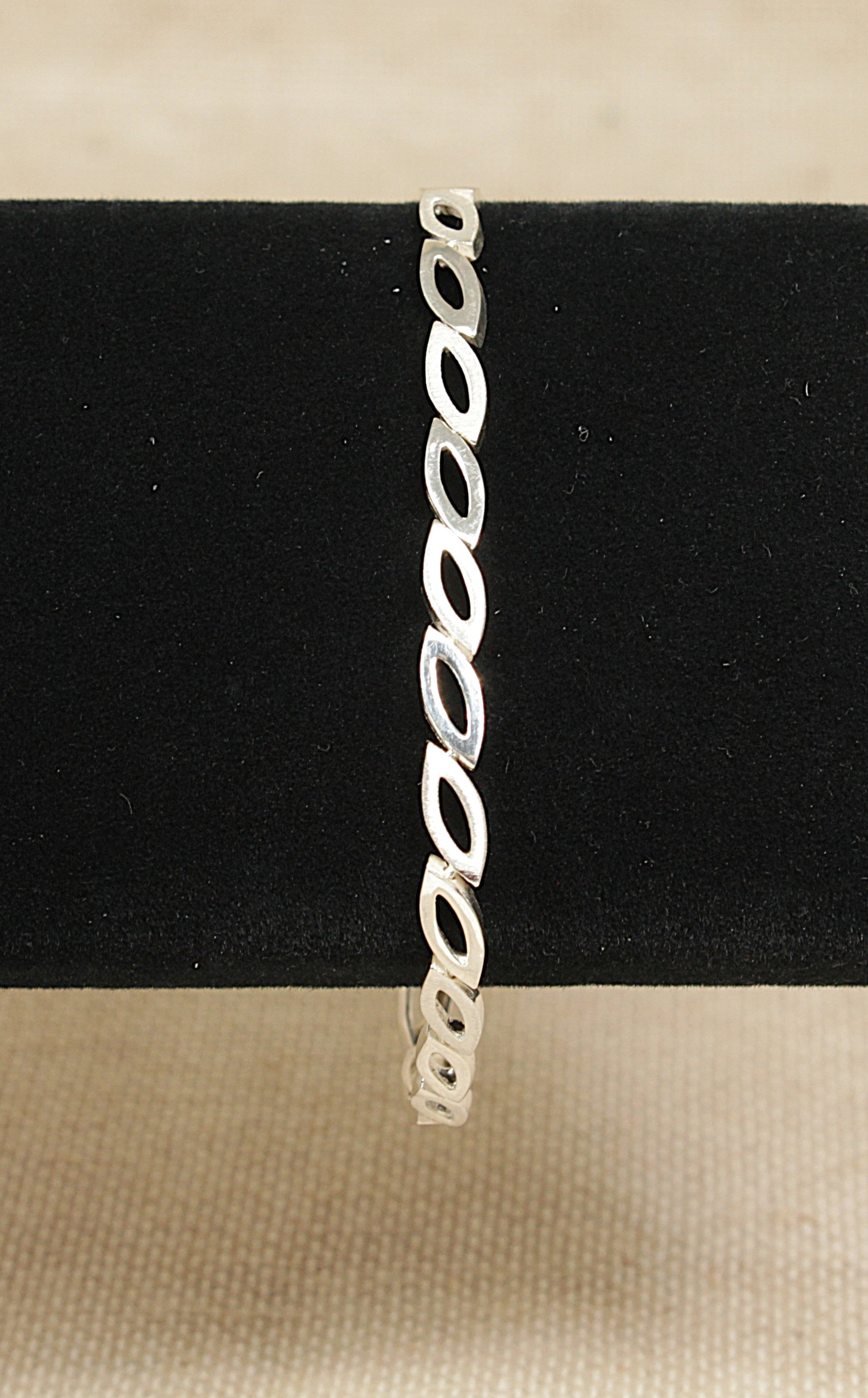 Silver bracelet on a black stand with a beige background