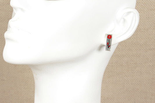 Silver earring displaying a red poppy on a mannequin ear with a beige background