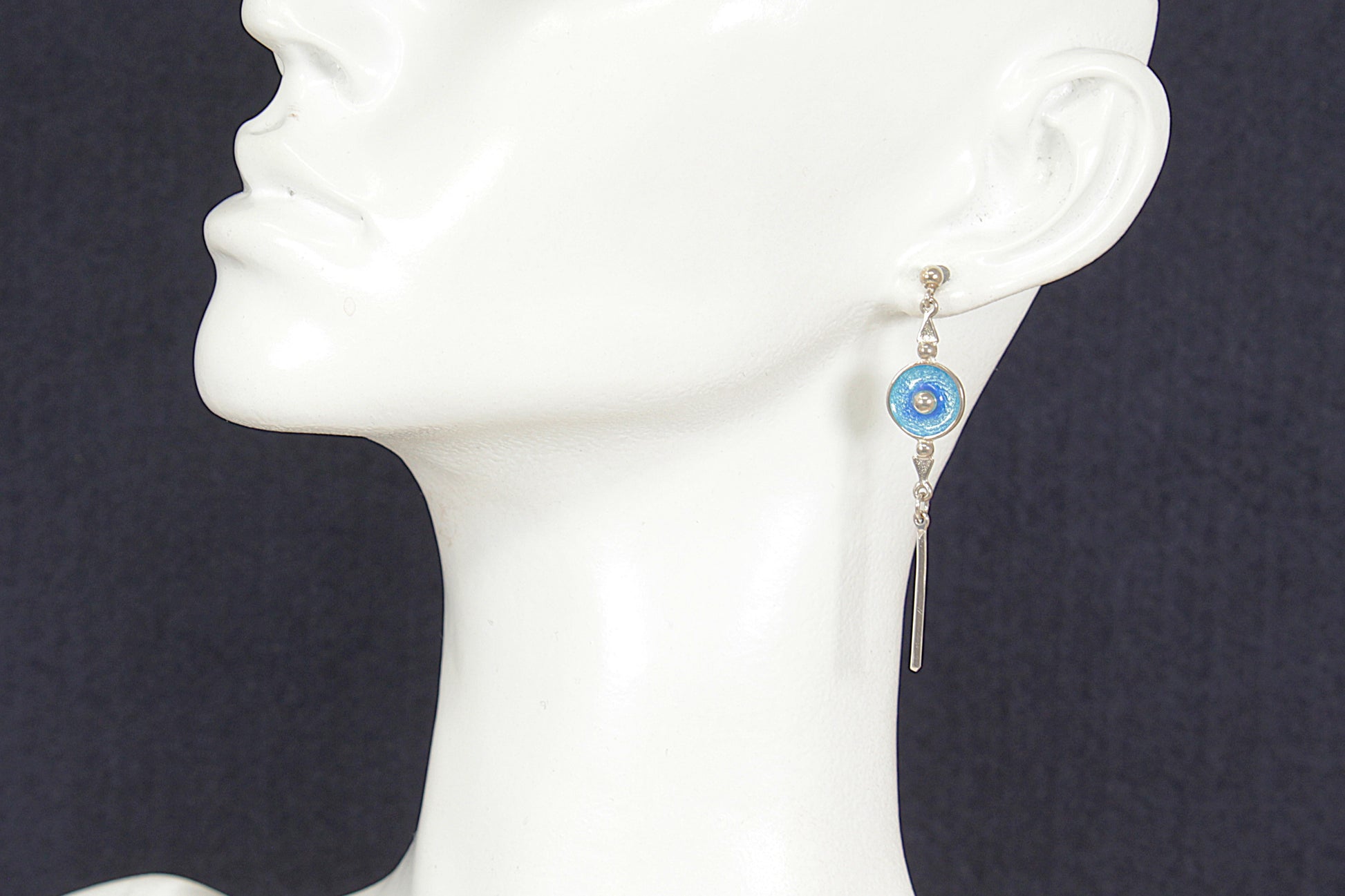 Earring with blue gemstone on a mannequin ear against a dark background
