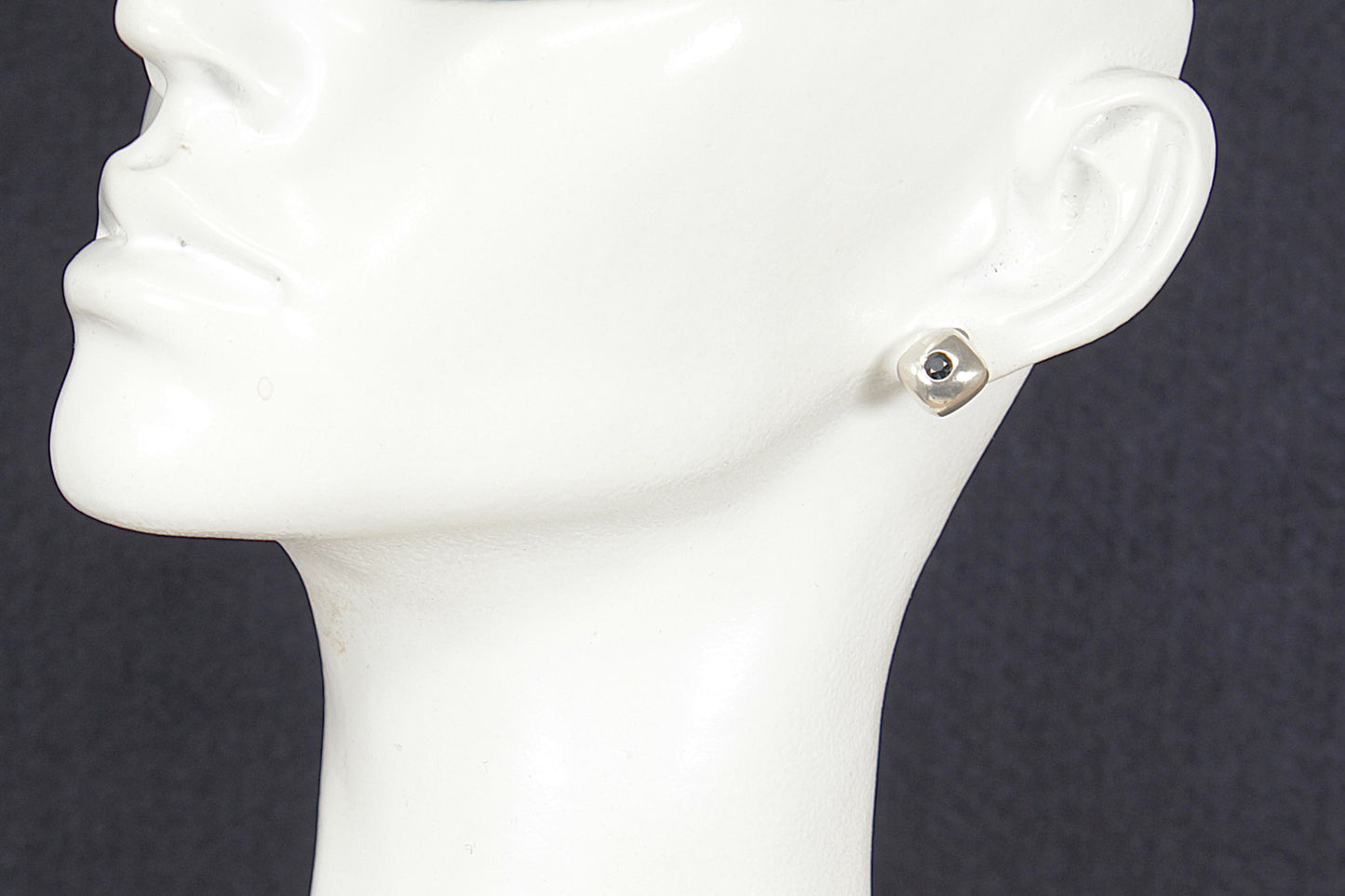Silver earring on a white mannequin ear against a dark background