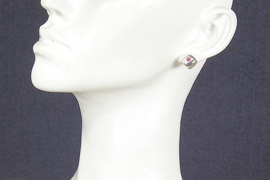 White mannequin head with a silver ruby earring on a dark background