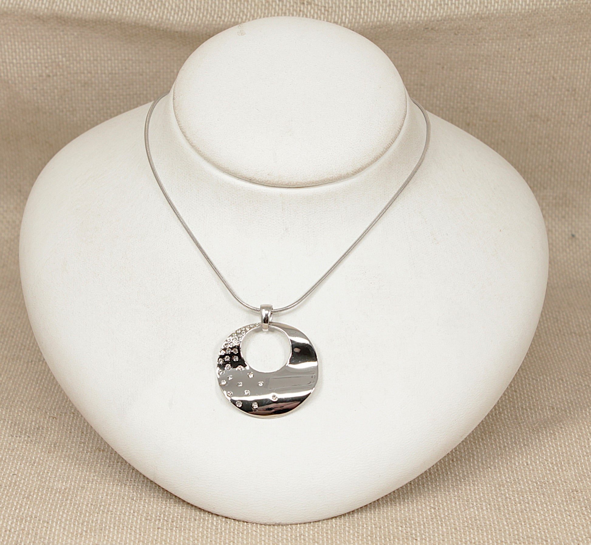 Silver necklace with a round pendant on a white stand against a beige background