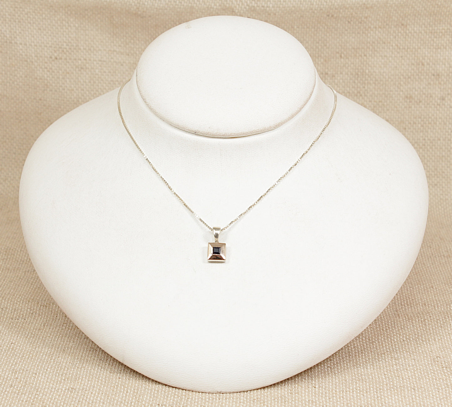 Silver necklace with a sapphire pendant on a white mannequin bust against a beige background