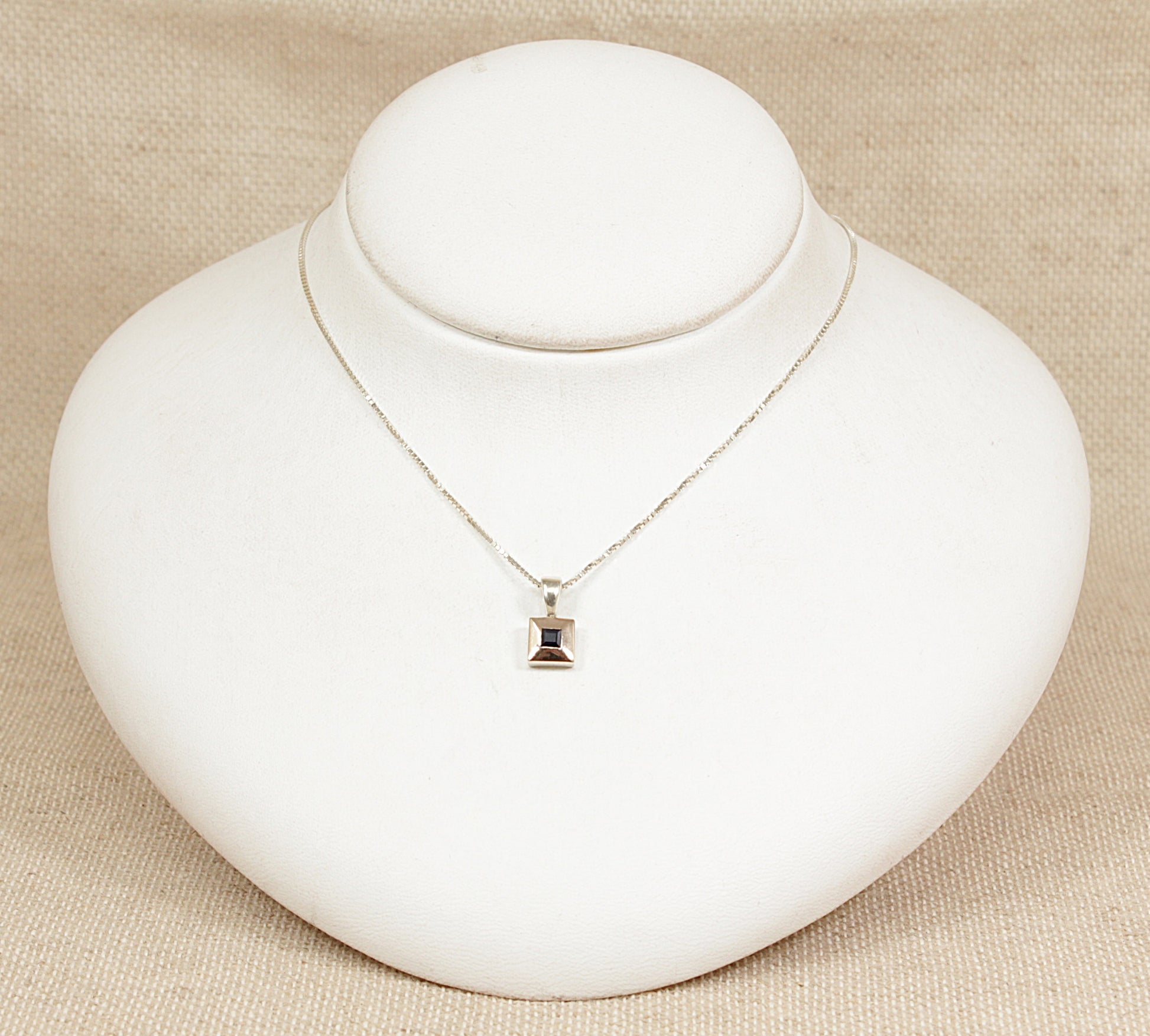 Silver necklace with a sapphire pendant on a white mannequin bust against a beige background
