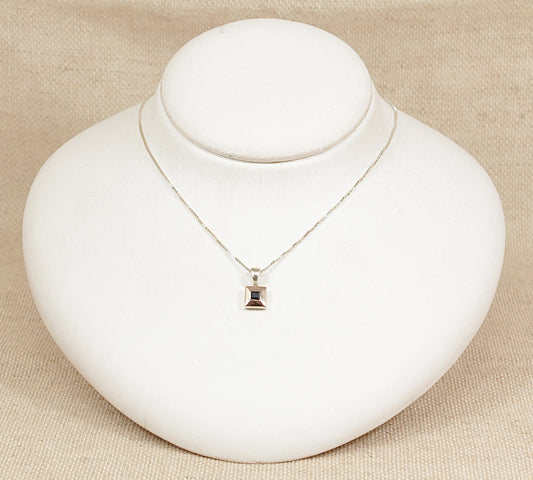 Silver necklace with a sapphire pendant on a white mannequin bust against a beige background