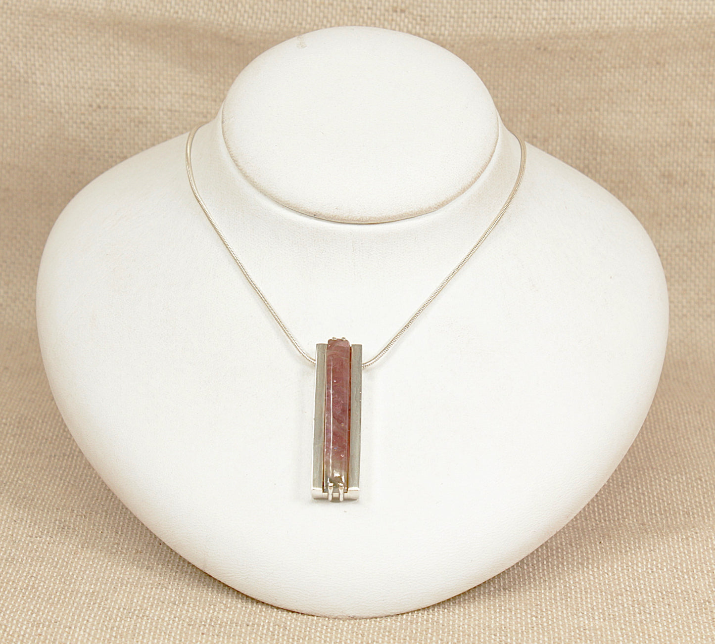 Necklace with a pink tourmaline pendant on a white bust against a beige background