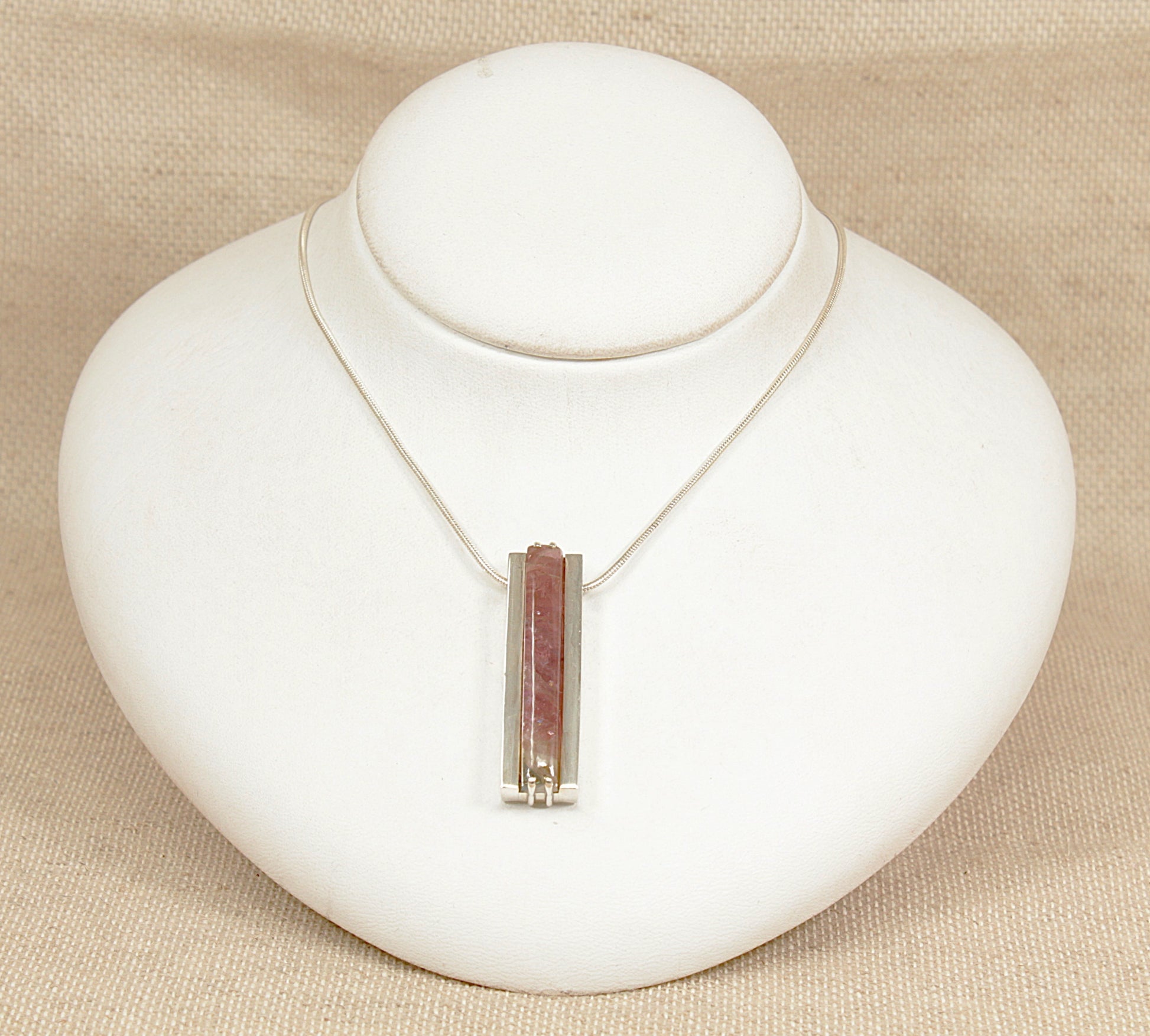 Necklace with a pink tourmaline pendant on a white bust against a beige background
