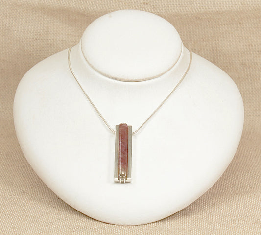 Necklace with a pink tourmaline pendant on a white bust against a beige background